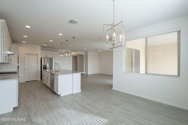 kitchen featuring white cabinetry, an island with sink, appliances with stainless steel finishes, and decorative light fixtures