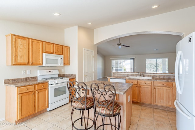 kitchen featuring ceiling fan, a kitchen island, white appliances, a breakfast bar area, and light tile patterned floors