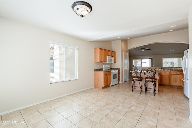 kitchen featuring ceiling fan, a breakfast bar, light tile patterned flooring, white appliances, and stone countertops