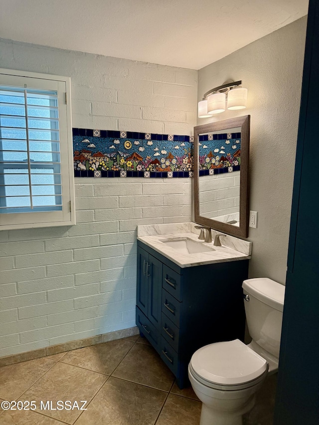 bathroom with toilet, vanity, tile patterned flooring, and brick wall