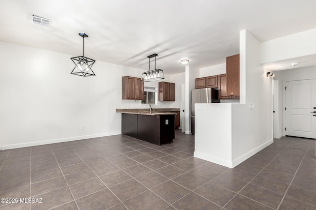 kitchen featuring sink, stainless steel refrigerator, hanging light fixtures, dark tile patterned floors, and dark brown cabinets