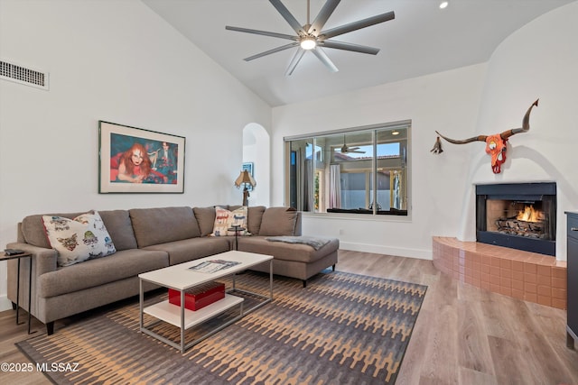 living room featuring hardwood / wood-style flooring, high vaulted ceiling, a large fireplace, and ceiling fan