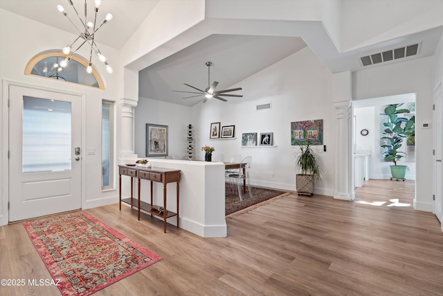 entryway featuring ceiling fan with notable chandelier, high vaulted ceiling, decorative columns, and light wood-type flooring