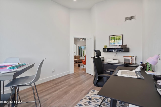 home office featuring a towering ceiling, ceiling fan, and light wood-type flooring