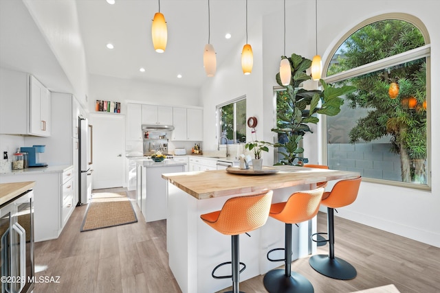 kitchen with white cabinetry, hanging light fixtures, a center island, beverage cooler, and light wood-type flooring