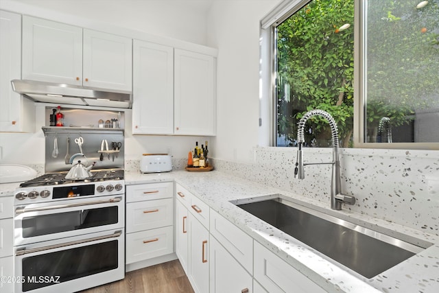 kitchen with double oven range, light stone countertops, sink, and white cabinets