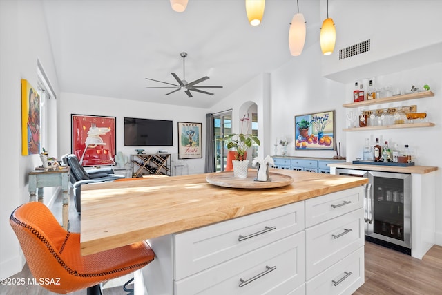 bar with pendant lighting, butcher block counters, white cabinets, beverage cooler, and light wood-type flooring