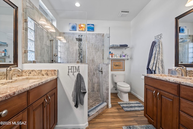 bathroom with hardwood / wood-style flooring, vanity, toilet, and a tile shower