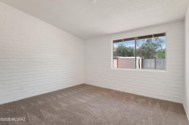 unfurnished room with vaulted ceiling, brick wall, and carpet floors