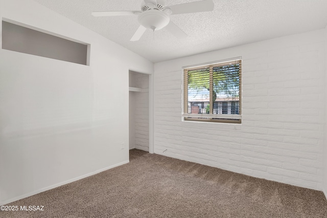 unfurnished bedroom with ceiling fan, carpet floors, a textured ceiling, a closet, and brick wall