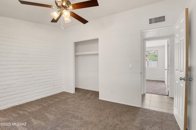 unfurnished bedroom with ceiling fan, brick wall, a closet, and light colored carpet