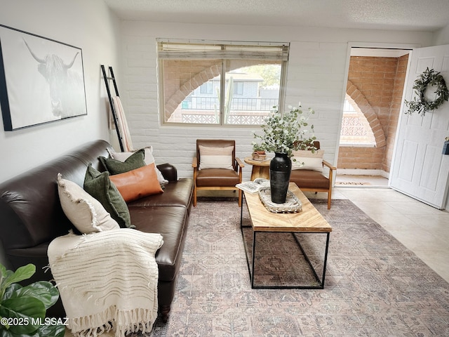 tiled living room featuring a textured ceiling and brick wall