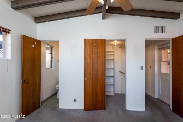 unfurnished bedroom with vaulted ceiling with beams, ensuite bath, multiple windows, and dark colored carpet