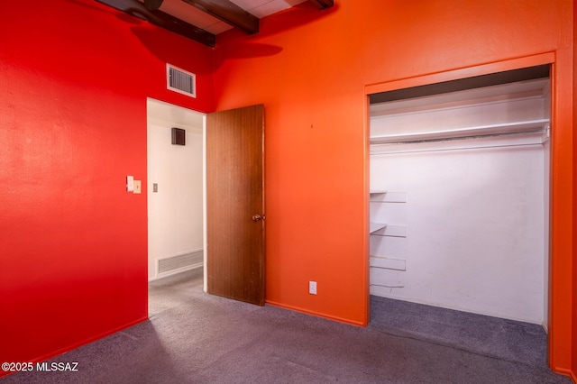 unfurnished bedroom with carpet flooring, beam ceiling, and a closet