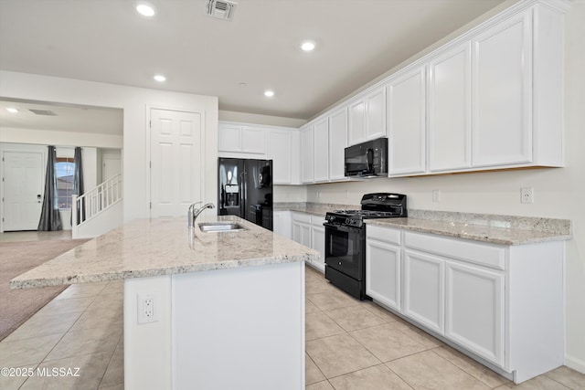 kitchen with sink, light stone counters, black appliances, white cabinets, and a center island with sink