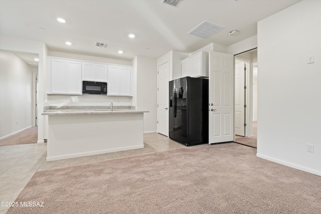 kitchen with white cabinetry, light stone countertops, black appliances, a center island with sink, and light carpet