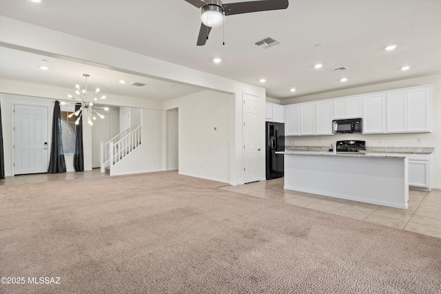 kitchen featuring ceiling fan with notable chandelier, an island with sink, white cabinets, black appliances, and light carpet