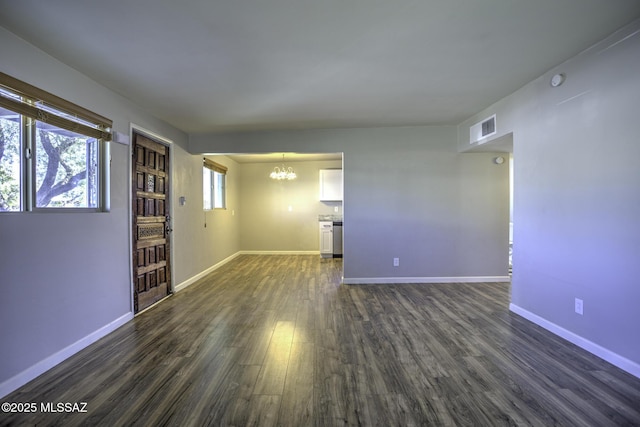 spare room featuring dark wood-type flooring, plenty of natural light, and an inviting chandelier