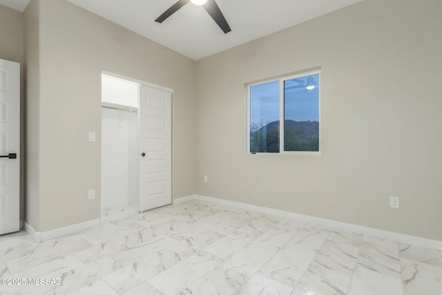 unfurnished bedroom featuring ceiling fan, marble finish floor, a closet, and baseboards