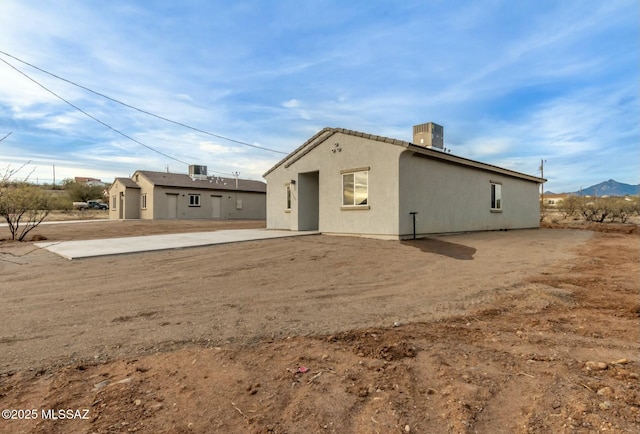 back of house featuring stucco siding, central AC, a mountain view, and a patio