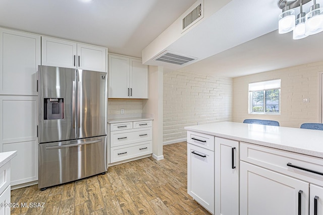 kitchen featuring brick wall, white cabinets, stainless steel fridge with ice dispenser, and light hardwood / wood-style flooring