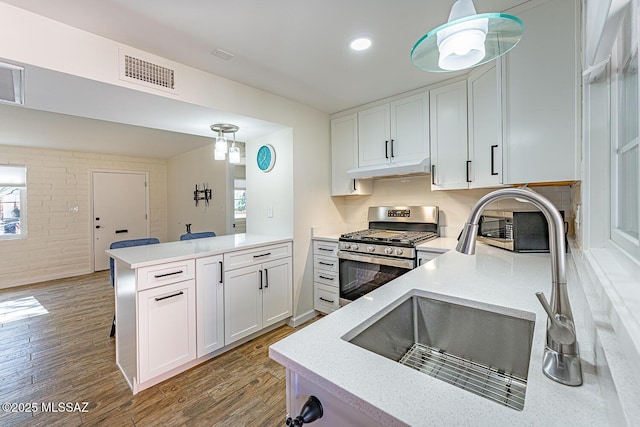 kitchen featuring white cabinetry, hardwood / wood-style flooring, gas range, pendant lighting, and sink