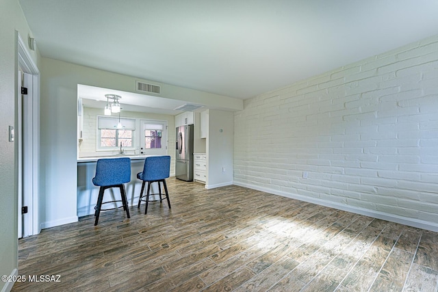 kitchen with brick wall, white cabinetry, stainless steel fridge with ice dispenser, kitchen peninsula, and a breakfast bar area