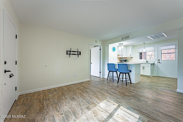 kitchen with a breakfast bar area, white cabinets, pendant lighting, light hardwood / wood-style flooring, and sink