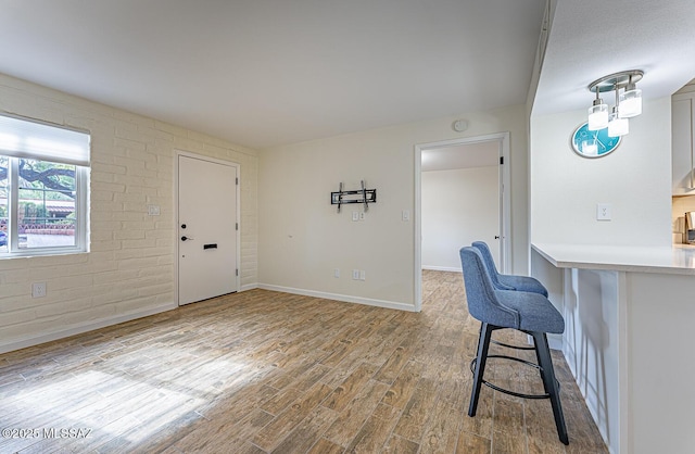 interior space with brick wall, light hardwood / wood-style flooring, and a breakfast bar area