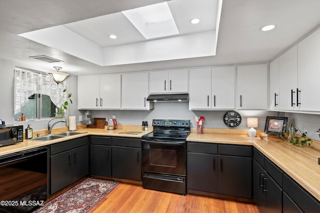 kitchen featuring black appliances, white cabinetry, sink, a raised ceiling, and light hardwood / wood-style flooring