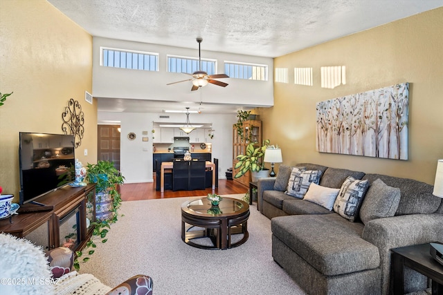 living room with hardwood / wood-style flooring, a textured ceiling, a towering ceiling, and ceiling fan