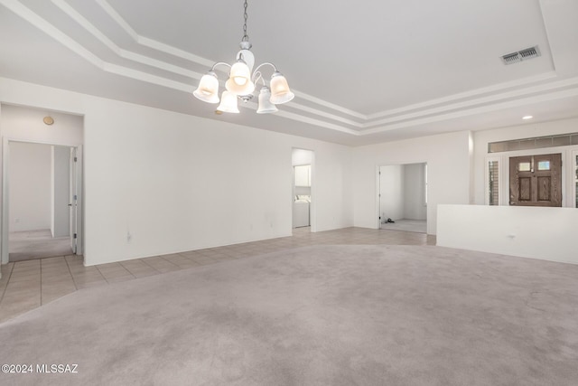 carpeted spare room with an inviting chandelier, a tray ceiling, and washer / dryer