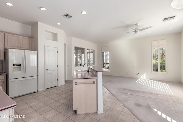 kitchen featuring white refrigerator with ice dispenser, sink, ceiling fan, light tile patterned floors, and a center island with sink