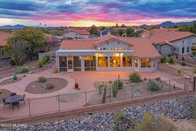 back house at dusk with a sunroom, a mountain view, and a patio