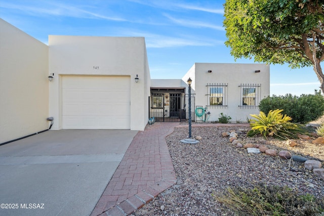 adobe home with driveway, a garage, a gate, and stucco siding