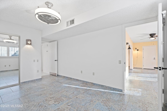 unfurnished room with a textured ceiling, ceiling fan, visible vents, and baseboards