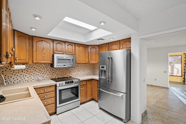 kitchen featuring stainless steel appliances, a sink, light countertops, backsplash, and brown cabinetry