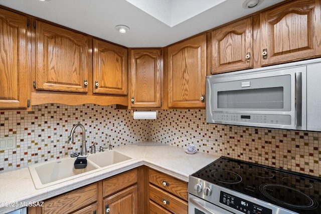 kitchen featuring tasteful backsplash, tile counters, brown cabinets, stainless steel appliances, and a sink