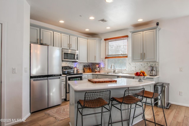 kitchen featuring appliances with stainless steel finishes, a kitchen island, sink, light wood-type flooring, and a breakfast bar