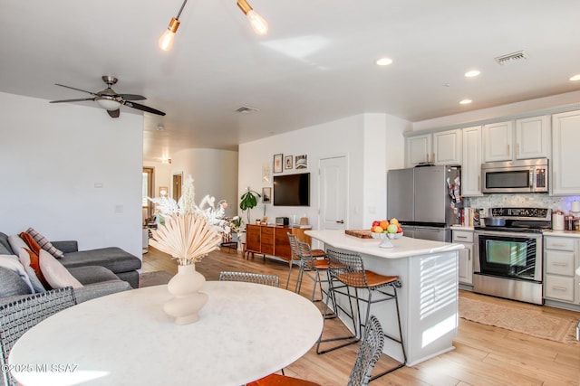 kitchen featuring a kitchen bar, ceiling fan, appliances with stainless steel finishes, tasteful backsplash, and a center island