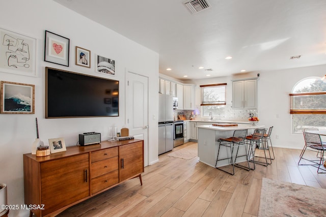 kitchen featuring white cabinetry, decorative backsplash, a kitchen breakfast bar, a kitchen island, and light hardwood / wood-style flooring