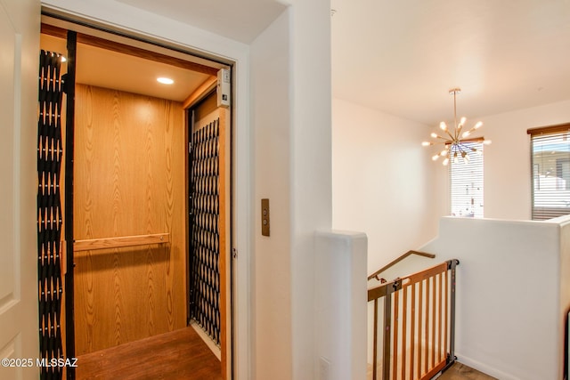 hallway with a notable chandelier, hardwood / wood-style flooring, and elevator