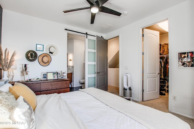 bedroom with a spacious closet, light carpet, a closet, ceiling fan, and a barn door