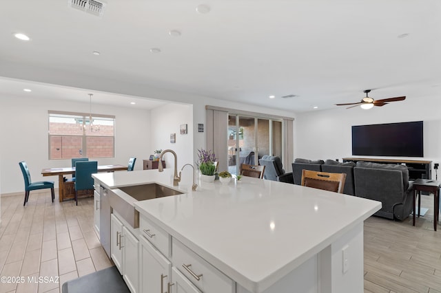 kitchen featuring visible vents, white cabinets, an island with sink, light countertops, and a sink