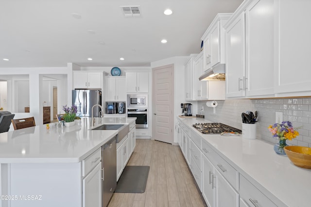 kitchen featuring light countertops, decorative backsplash, appliances with stainless steel finishes, a sink, and under cabinet range hood