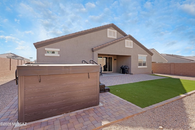 rear view of property with a patio, a fenced backyard, a lawn, stucco siding, and a hot tub