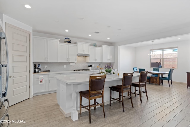 kitchen with white cabinets, light countertops, a kitchen island with sink, and under cabinet range hood