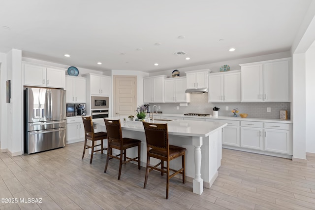 kitchen featuring an island with sink, appliances with stainless steel finishes, a kitchen breakfast bar, under cabinet range hood, and white cabinetry