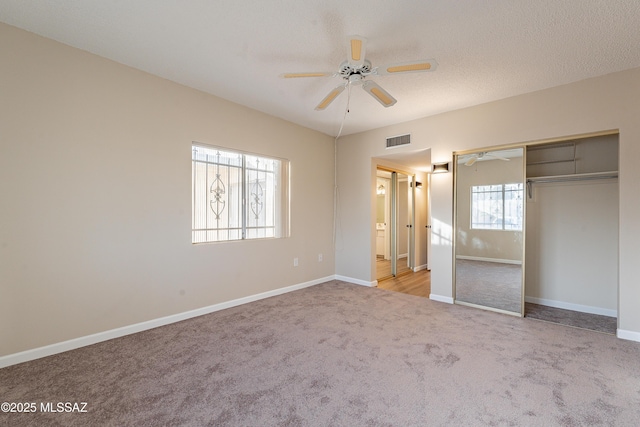 unfurnished bedroom with light carpet, a textured ceiling, ceiling fan, and a closet