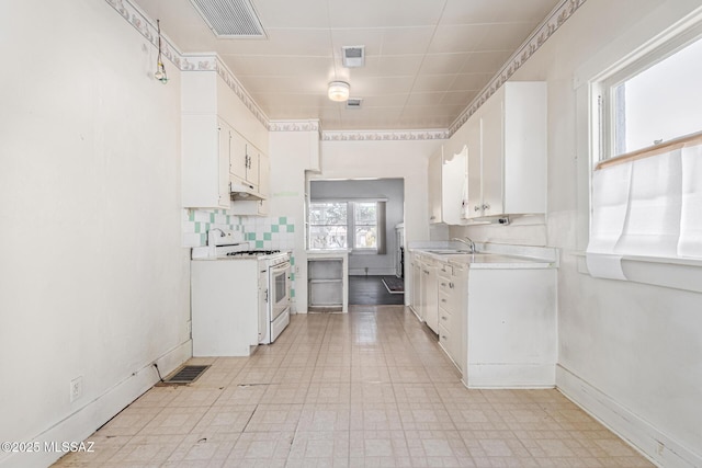 kitchen with white cabinetry, backsplash, white gas range oven, and sink